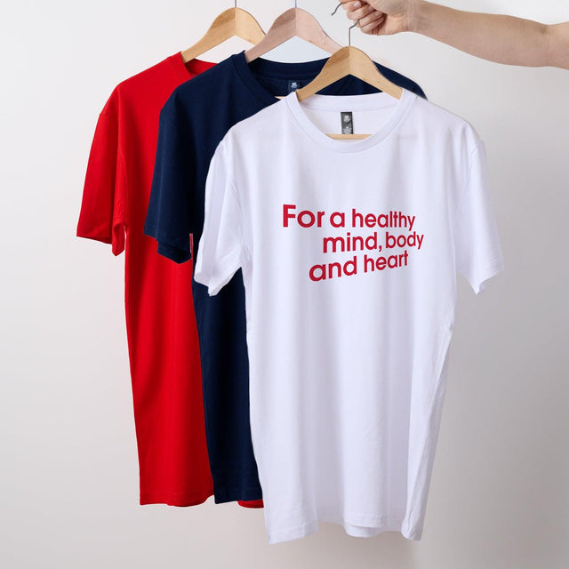 Three t-shirts hanging on hooks, next to each other. From left to right: red, navy blue, and white. Featuring the slogan For a healthy mind, body and heart.