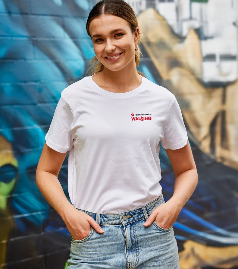 Woman wearing a white Heart Foundation t-shirt with red text standing in front of a colorful mural.