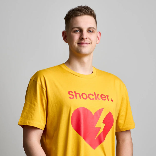 Person wearing a yellow t-shirt with a red heart and lightning bolt design, and the word 'Shocker' on a plain background.