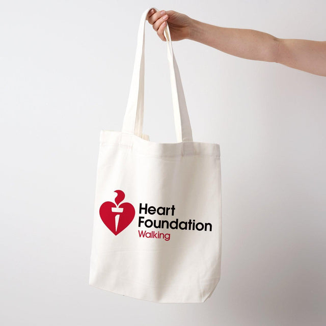 Extended arm holding a cream cotton canvas tote bag featuring Heart Foundation Walking logo.