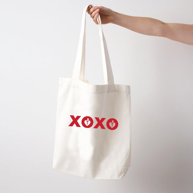 Heart Foundation white canvas tote bag shown held in hand with XOXO design in red print on the front.