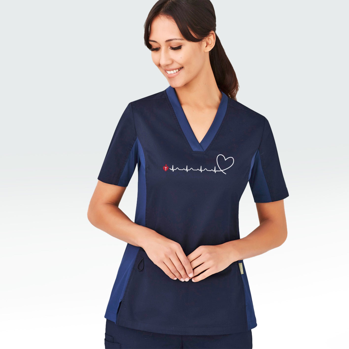 Model wearing a women's navy scrub top featuring heartbeat line across front chest ending with stylised heart shape and incorporating Heart Foundation brand mark.