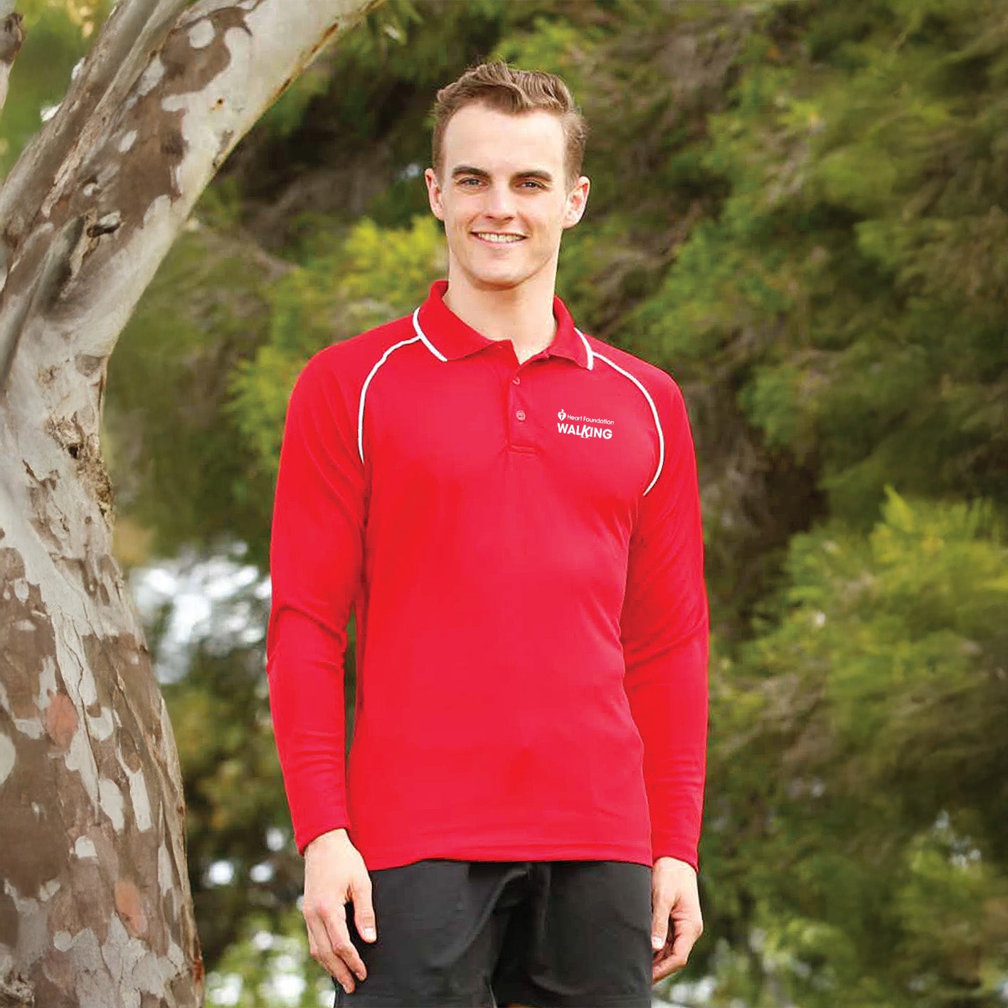 Young man in outdoor setting modelling Heart Foundation Walking's red long sleeved polo shirt, showing white collar accents on raglan sleeve seam and collar.