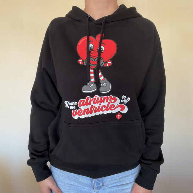 Person wearing a black hoodie with a cartoon heart design and text on a plain background