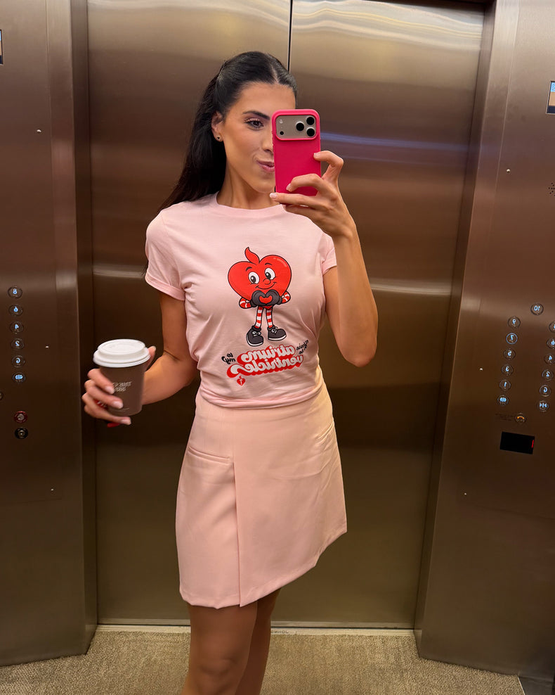 Woman taking a mirror selfie in an elevator wearing a pink t-shirt with a cartoon character and text.