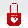 A red canvas tote bag with two top handles, featuring the word 'Shocker' in white above a large white broken-heart graphic with a red lightning bolt, shown on a light gray gradient background.