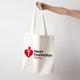 Extended arm holding a cream cotton canvas  tote bag featuring Heart Foundation Walking logo.