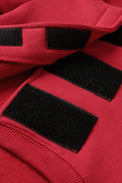 Close-up of a red fleece item with three black hook-and-loop velcro patches on the opening.