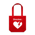 A red tote bag with a white graphic on the front featuring the word 'Shocker' and a broken heart with a lightning bolt inside, shown against a light gray gradient.