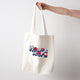 Heart Foundation cream canvas tote bag shown held in hand with vintage look Heart hero text in red and blue print on the front.